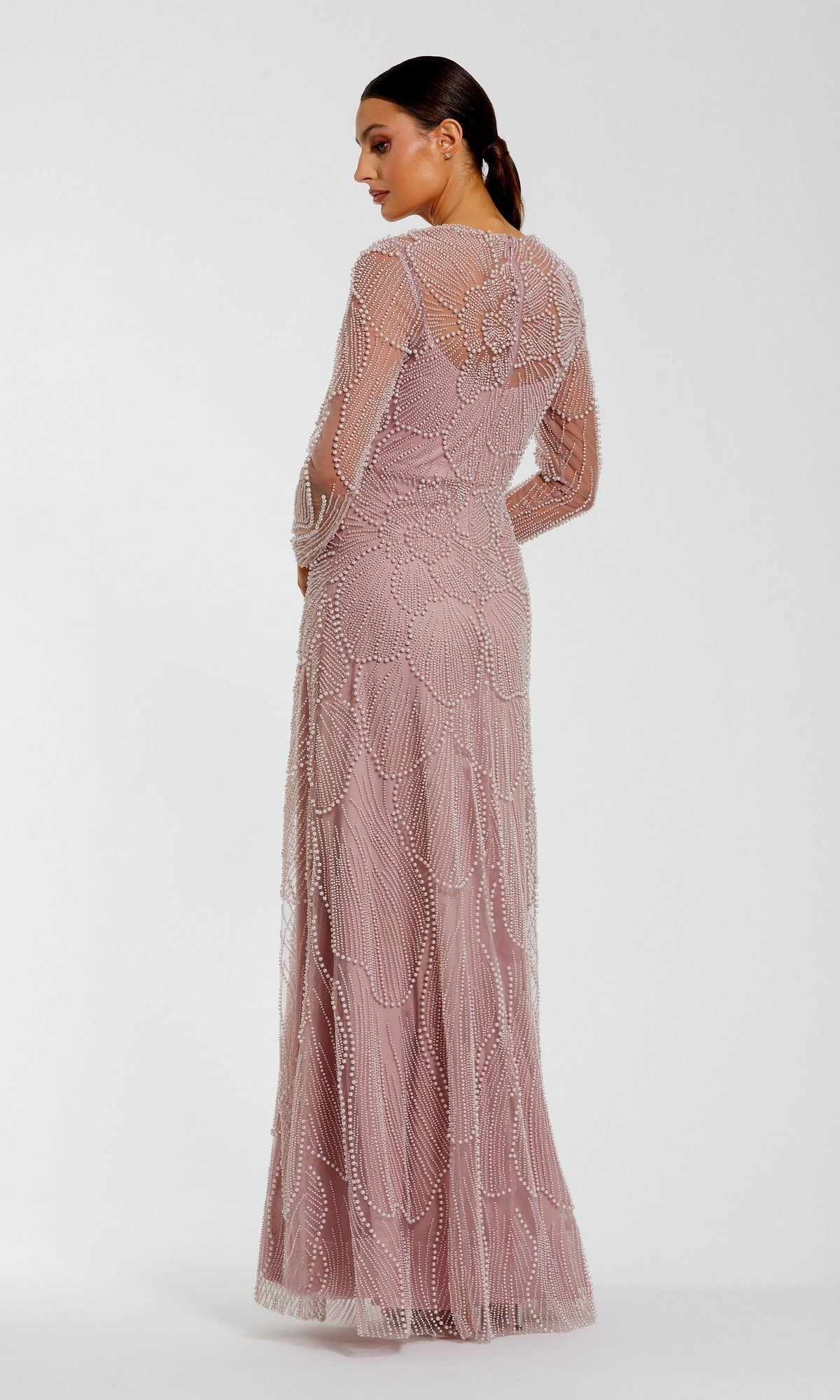 Wearing the Mac Duggal 69012, a woman stands with her back to the camera, highlighting the exquisite pearl beading and intricate detailing on the back and sleeves of this long, blush-colored formal dress against a simple background.
